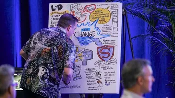 Matt standing in front of a small panel at a client conference.  He's drawing the content in a graphic recording manner.