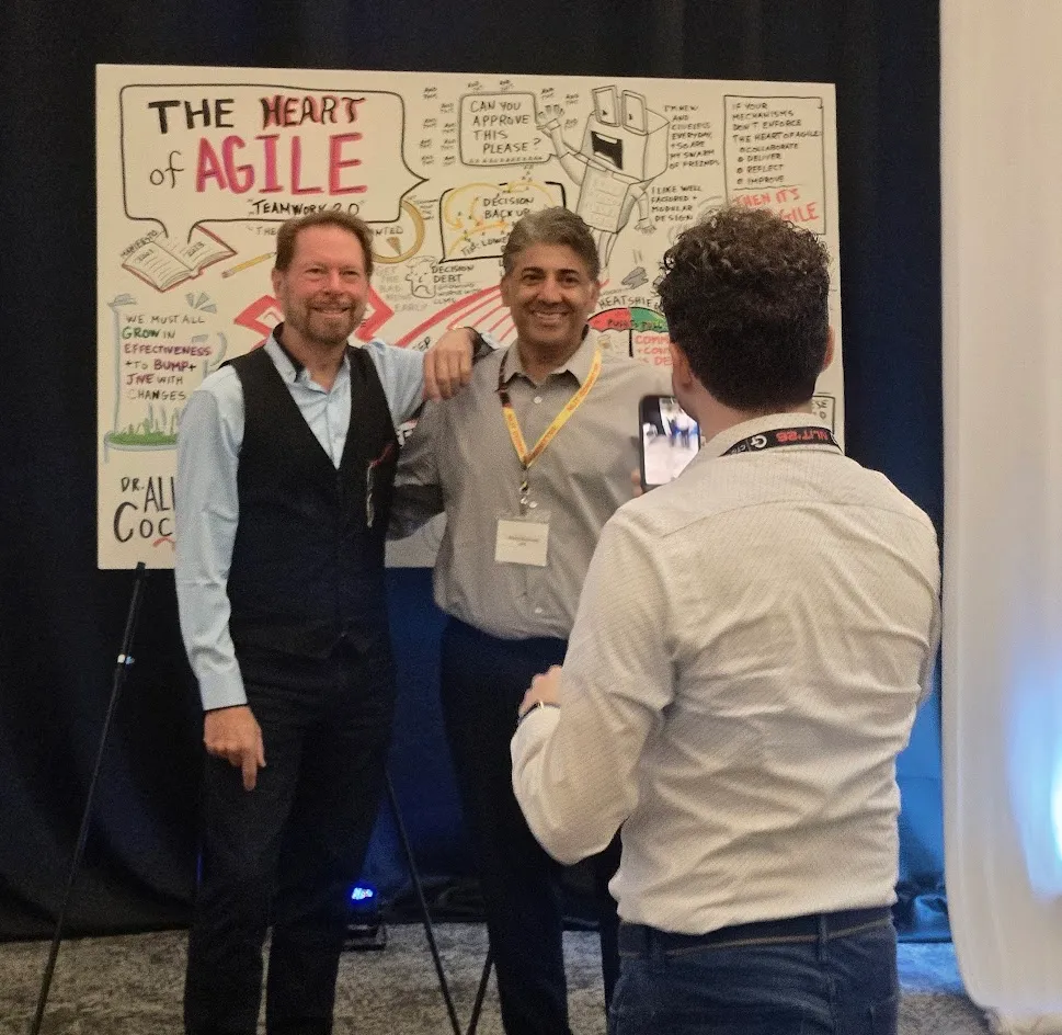Keynote speaker and event participant standing in front of a graphic created in real time during the keynote.  Another audience member taking a photo