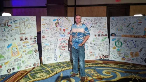 Matt Orley in a Hawaiian shirt standing in front of illustrations at a restaurant technology conference.