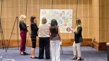 Event attendees reviewing a graphic recording between conference sessions.  Wide room, this panel was placed near the stage.